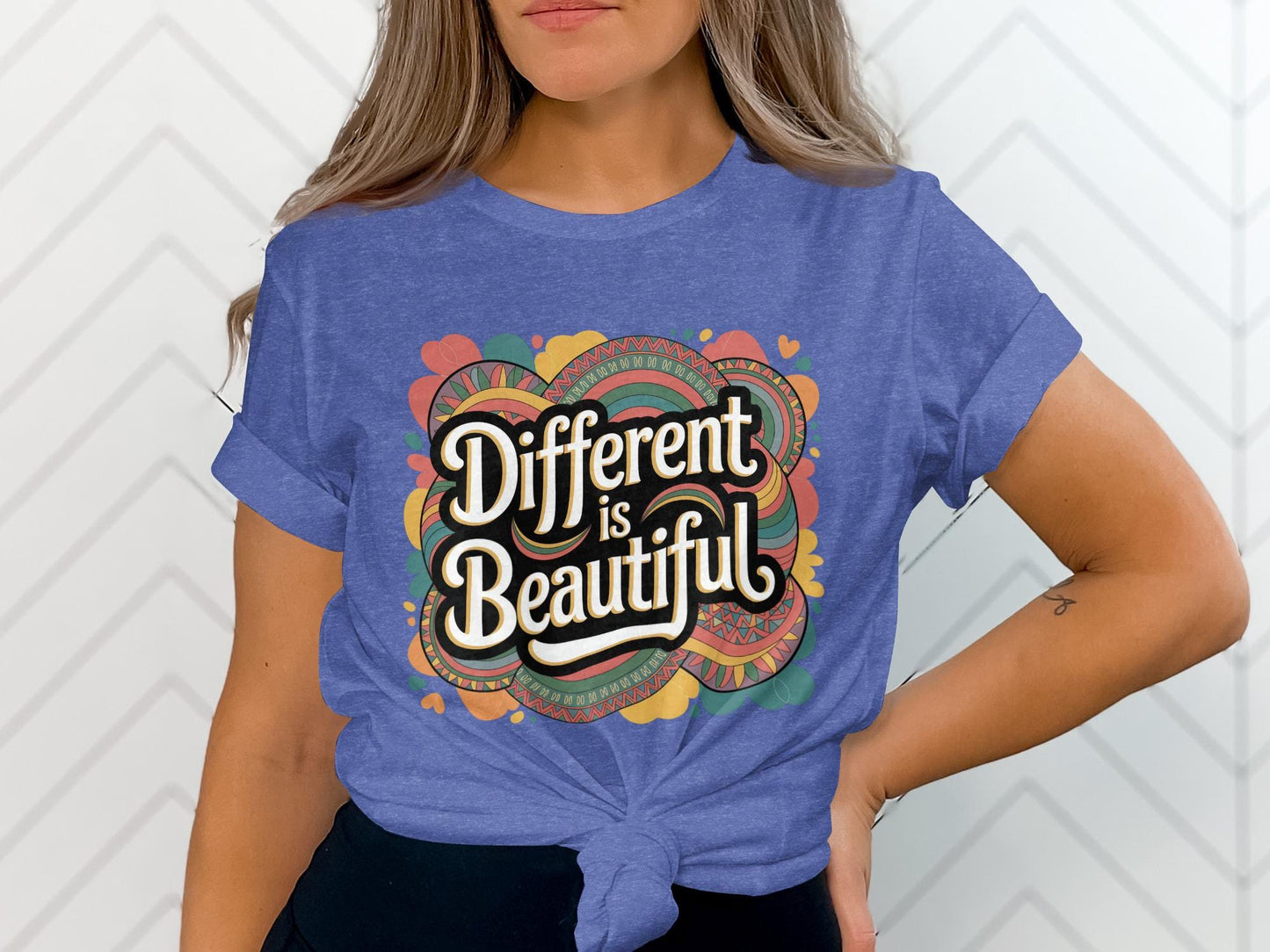 Woman wearing a tied royal blue t-shirt with a vibrant retro design that reads “Different is Beautiful” in large white lettering. The design includes colorful swirls, hearts, and patterns in pink, yellow, teal, and orange. This colorful graphic tee is a bold shirt, perfect as a positive quote tee, emotional shirt, and self love t shirt. A custom graphic print that works as a unique statement tee, colorful design tee, and inspirational shirt for those who love a stand out shirt.