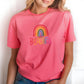Close-up of a pink t-shirt with rainbow “BEAUTIFUL” design worn by a woman with blonde hair, posing in front of a clean white background.