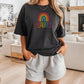 Woman wearing a black t-shirt with a colorful rainbow and the word “BEAUTIFUL” in rainbow text, standing in a stylish modern living room.