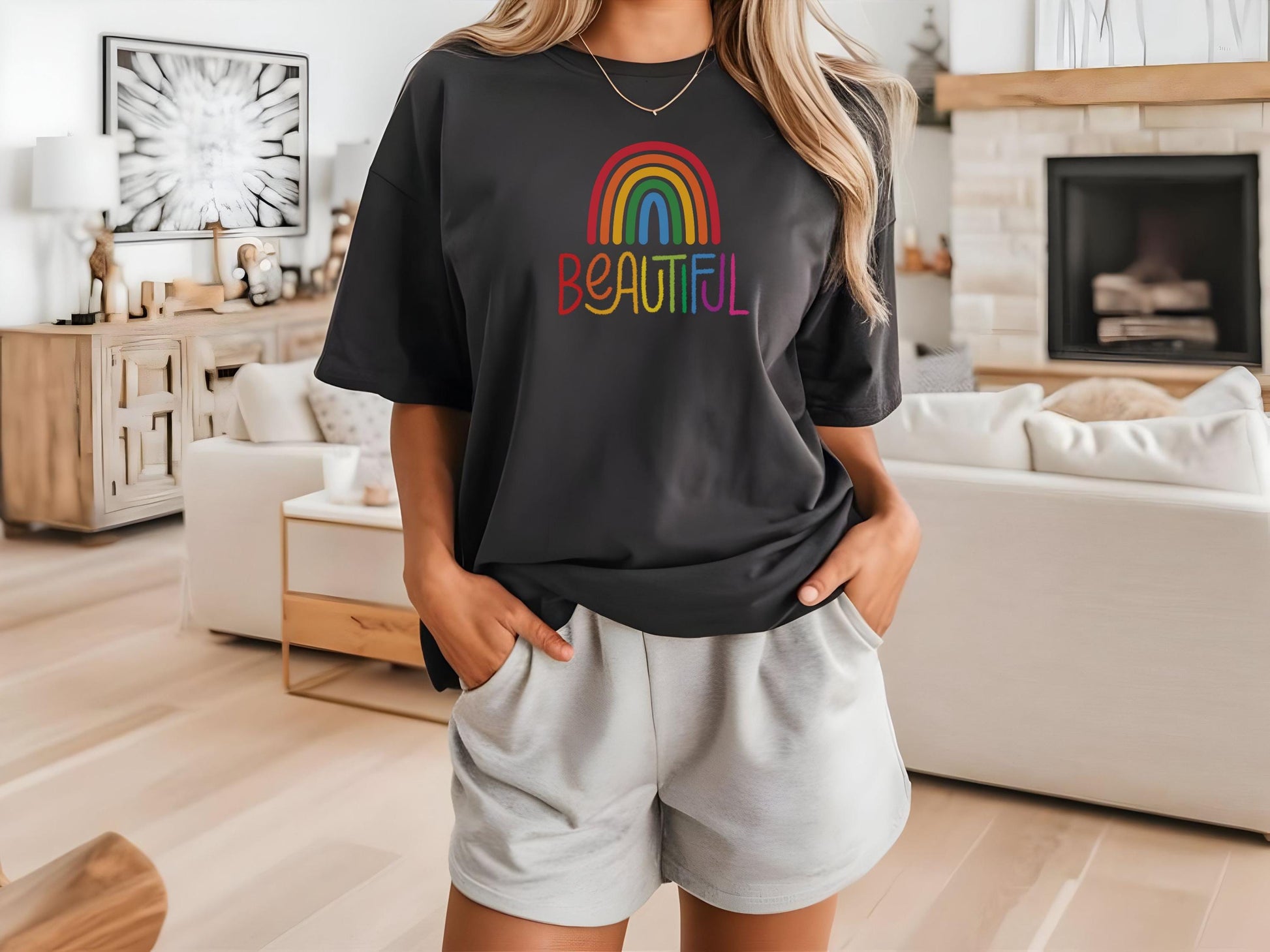 Woman wearing a black t-shirt with a colorful rainbow and the word “BEAUTIFUL” in rainbow text, standing in a stylish modern living room.