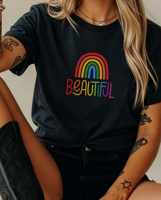 Black rainbow pride t-shirt with “Beautiful” text in rainbow colors, worn by a woman with arm tattoos. Queer fashion shirt, dark aesthetic pride apparel, colorful LGBTQ+ message tee.