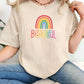 Cream beige t-shirt with rainbow “Beautiful” print, worn by woman in blue jeans. Neutral tone pride shirt, inclusive everyday wear, simple self-love tee for women.