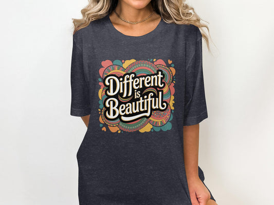 Woman wearing a dark heather gray t-shirt with a bold retro-style graphic that says &quot;Different is Beautiful&quot; in white lettering. The design features colorful, groovy 70s-inspired shapes and patterns in pink, teal, orange, yellow, and green. The shirt has a relaxed fit and short sleeves, perfect for spreading positive, inclusive vibes.